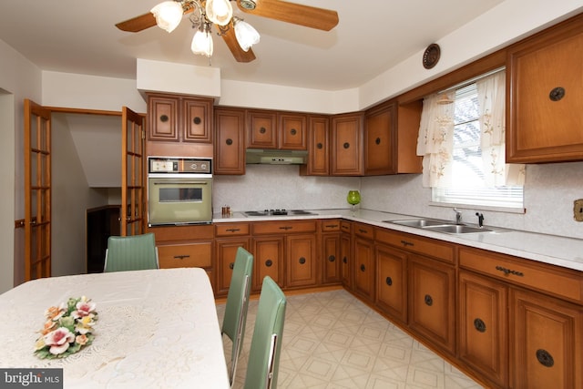 kitchen featuring oven, electric cooktop, under cabinet range hood, a sink, and light countertops