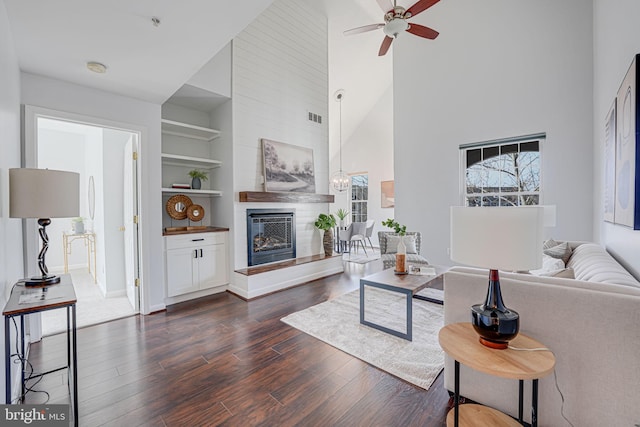 living area featuring built in features, dark wood-style floors, visible vents, high vaulted ceiling, and a fireplace