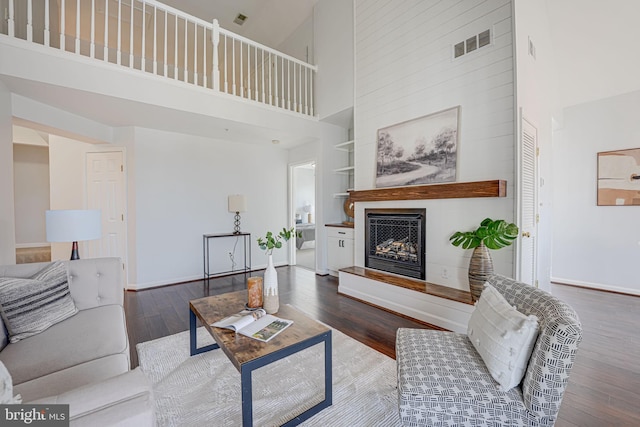 living area featuring visible vents, built in shelves, a fireplace with raised hearth, hardwood / wood-style flooring, and baseboards