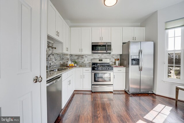 kitchen with light stone counters, dark wood-style flooring, a sink, appliances with stainless steel finishes, and tasteful backsplash