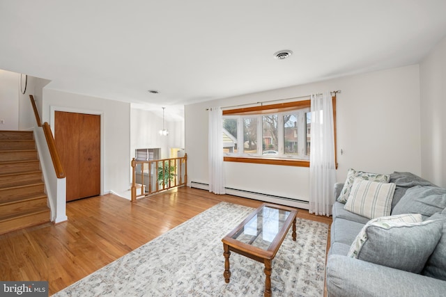 living room with baseboard heating, stairway, visible vents, and wood finished floors