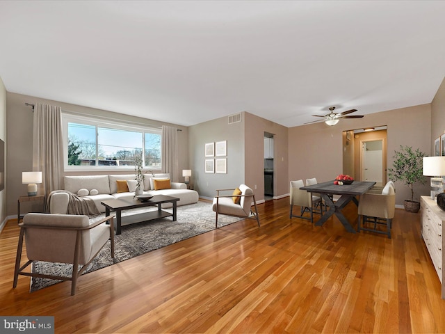 living area with light wood-style flooring, baseboards, visible vents, and ceiling fan