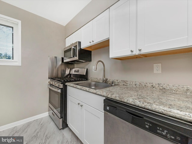 kitchen with baseboards, a sink, stainless steel appliances, white cabinets, and marble finish floor