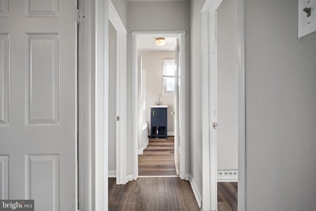 corridor featuring a baseboard heating unit, baseboards, and dark wood-style flooring