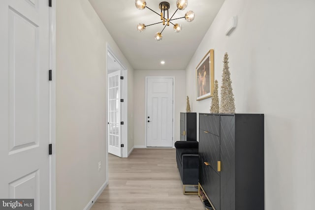 hallway with light wood-style flooring, baseboards, and a chandelier