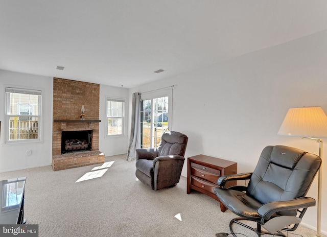 living area featuring visible vents, a healthy amount of sunlight, a brick fireplace, and carpet flooring