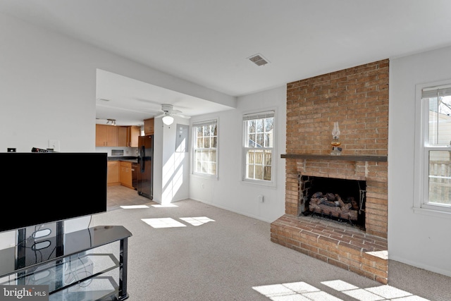 living area featuring a brick fireplace, plenty of natural light, visible vents, and light carpet