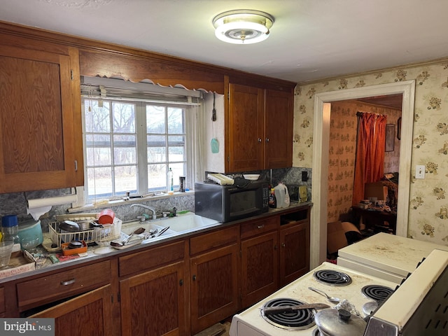 kitchen with electric stove, a sink, wallpapered walls, black microwave, and light countertops