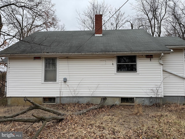 back of house with a chimney and a shingled roof