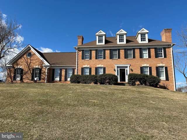 view of front of home featuring brick siding, a chimney, and a front lawn