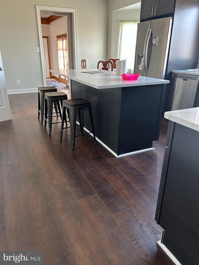 kitchen with dark wood-style floors, baseboards, a breakfast bar, stainless steel appliances, and light countertops