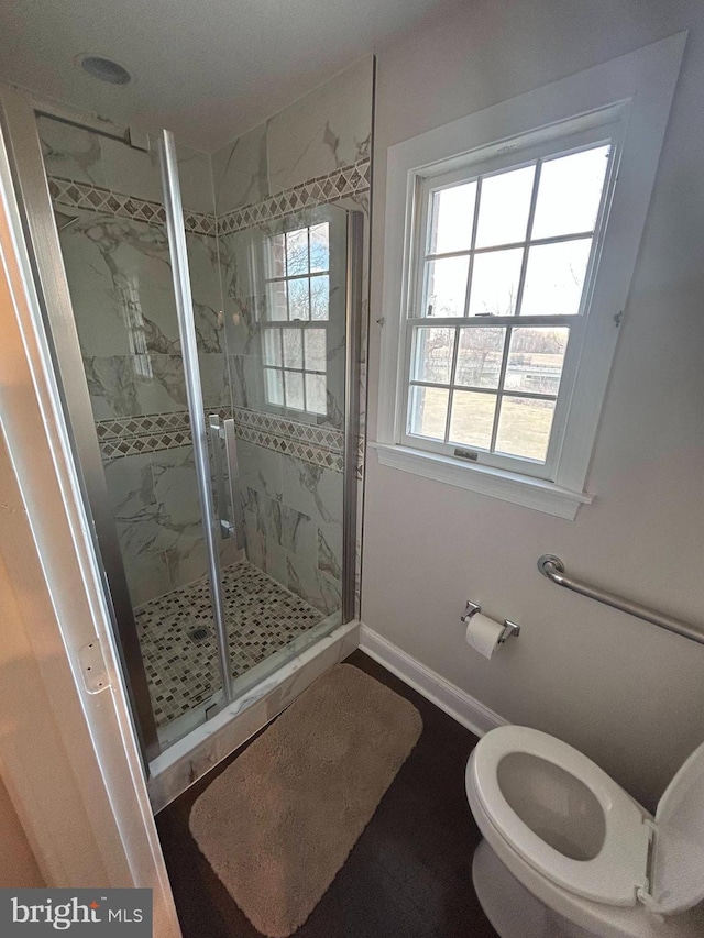 bathroom featuring a marble finish shower, a healthy amount of sunlight, toilet, and baseboards