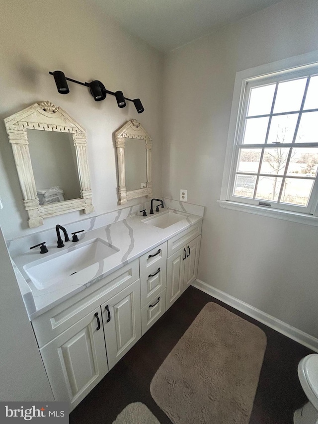 full bath with double vanity, wood finished floors, baseboards, and a sink