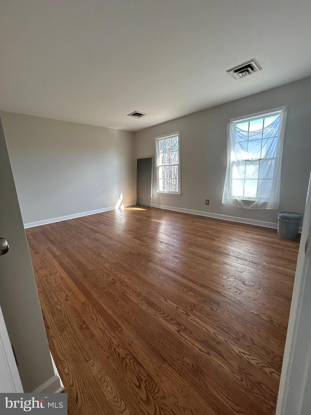 spare room with visible vents, baseboards, and dark wood-type flooring