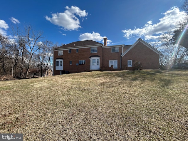 rear view of house with a yard, brick siding, and a chimney