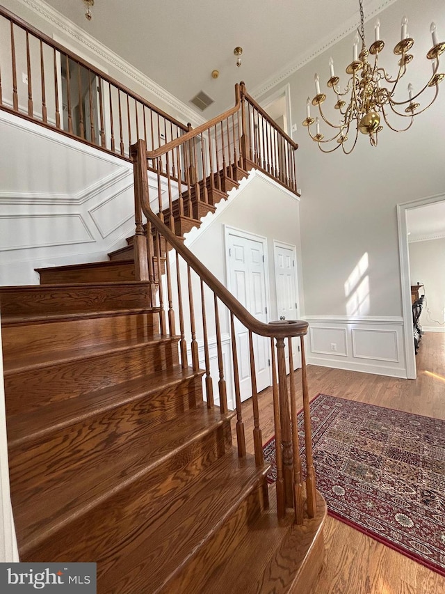 stairs with wainscoting, visible vents, ornamental molding, and wood finished floors