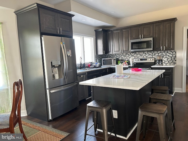 kitchen featuring a kitchen bar, backsplash, dark wood-style floors, stainless steel appliances, and light countertops