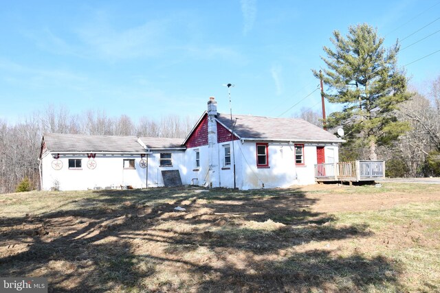 view of front of house with stucco siding, a front yard, a deck, and a chimney