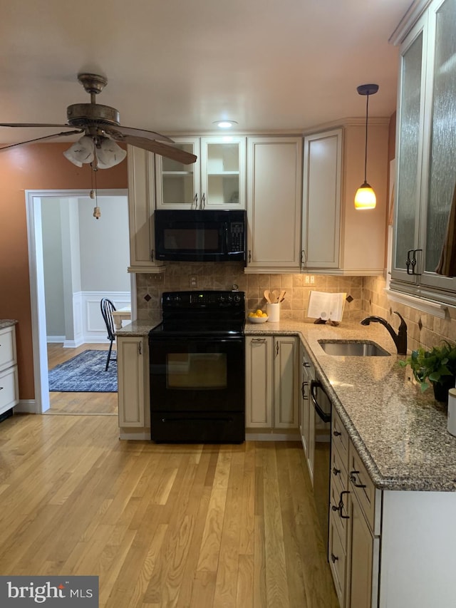 kitchen featuring light wood-type flooring, black appliances, a sink, tasteful backsplash, and light stone countertops