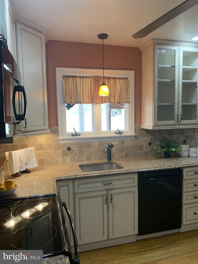 kitchen featuring light stone counters, a sink, black appliances, decorative light fixtures, and tasteful backsplash