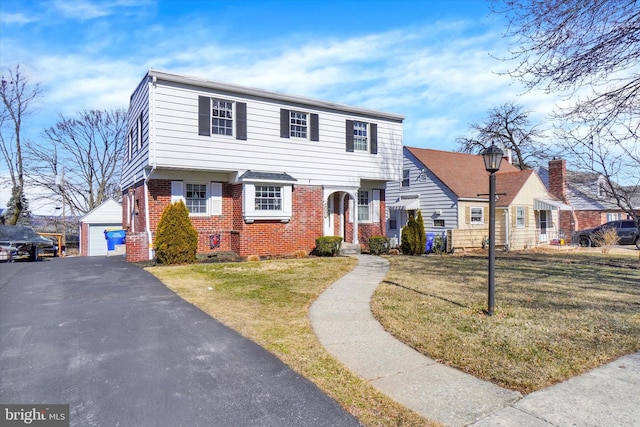 colonial home with an outdoor structure, a detached garage, brick siding, and a front yard