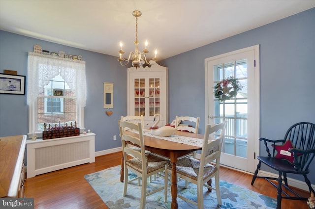 dining space featuring baseboards, radiator, an inviting chandelier, and wood finished floors