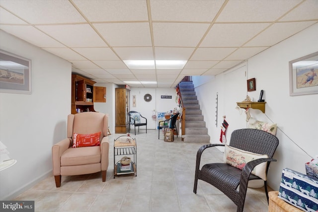 living area with light tile patterned floors, stairway, and a drop ceiling