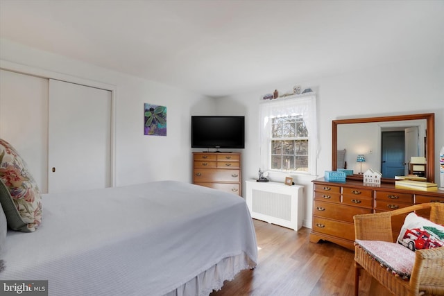 bedroom with a closet, radiator heating unit, and wood finished floors