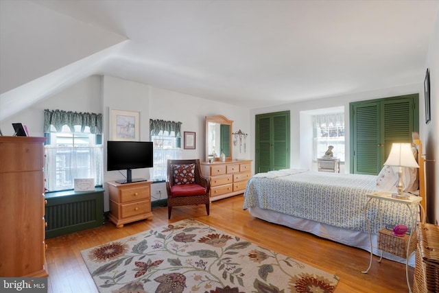 bedroom with vaulted ceiling, multiple windows, radiator, and hardwood / wood-style flooring