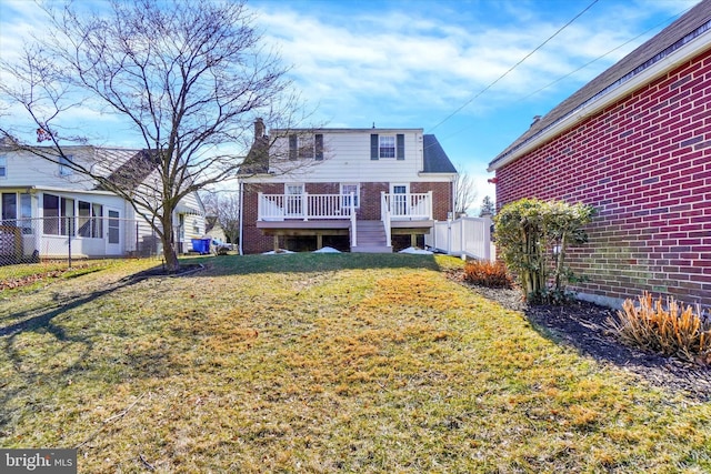 back of property featuring a deck, fence, a lawn, and brick siding