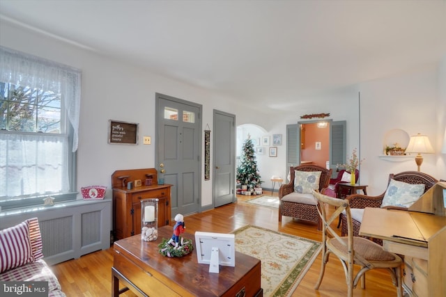 living area with arched walkways, light wood-style flooring, and radiator heating unit