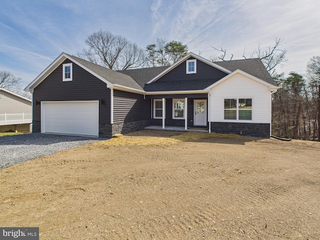 view of front facade featuring gravel driveway, covered porch, stone siding, and a shingled roof