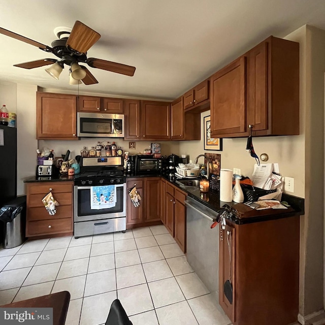 kitchen featuring brown cabinetry, light tile patterned flooring, a sink, stainless steel appliances, and dark countertops