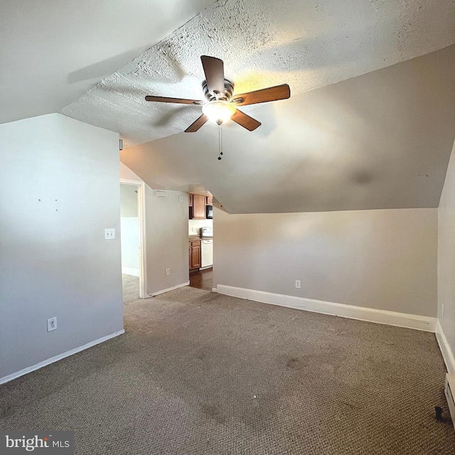 additional living space with dark carpet, a textured ceiling, baseboards, and vaulted ceiling