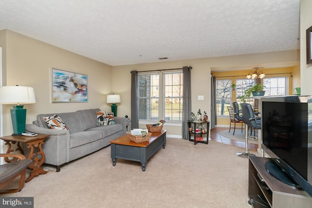 living room featuring baseboards, visible vents, a textured ceiling, light carpet, and a chandelier