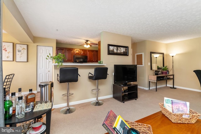 living room featuring light carpet, ceiling fan, a textured ceiling, and baseboards