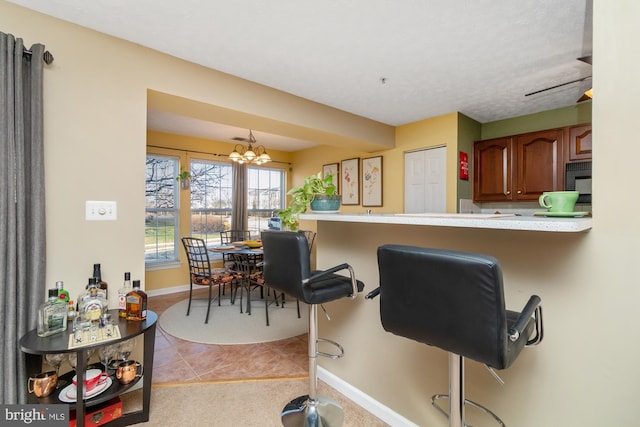 kitchen featuring light tile patterned floors, brown cabinetry, baseboards, light countertops, and a chandelier