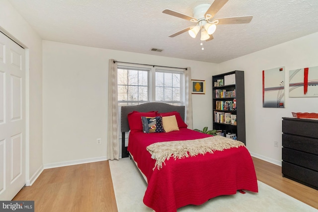 bedroom featuring visible vents, a ceiling fan, a textured ceiling, wood finished floors, and baseboards