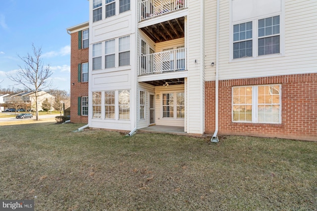 rear view of property featuring brick siding, a balcony, and a yard