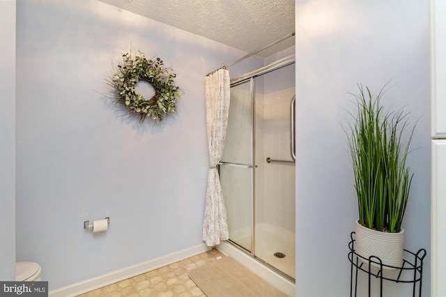 bathroom featuring toilet, a stall shower, a textured ceiling, and baseboards