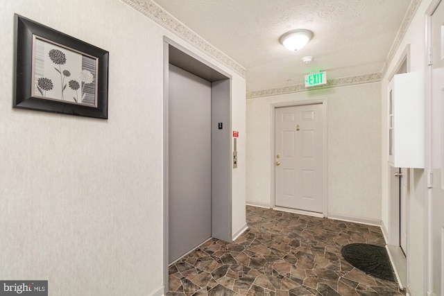 hall featuring elevator, a textured ceiling, stone finish flooring, and baseboards