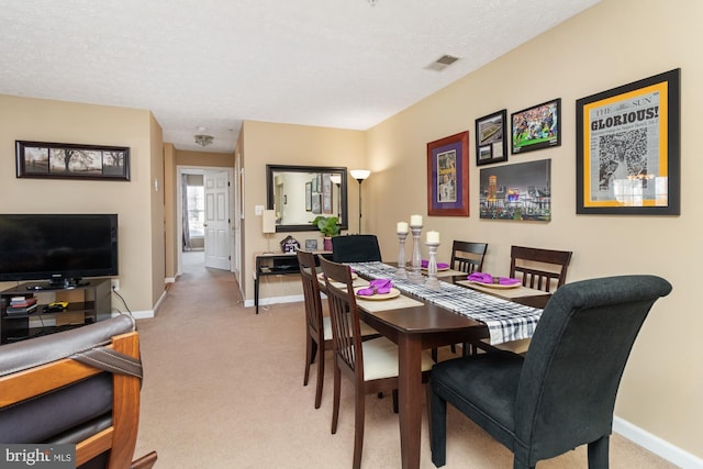 dining space with a textured ceiling, visible vents, baseboards, and light carpet