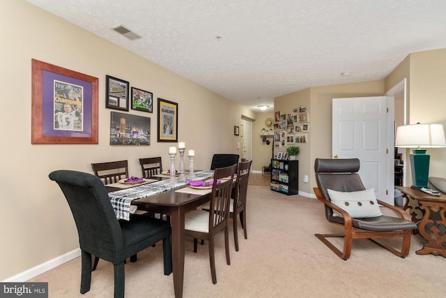 dining area with a textured ceiling, baseboards, visible vents, and light carpet