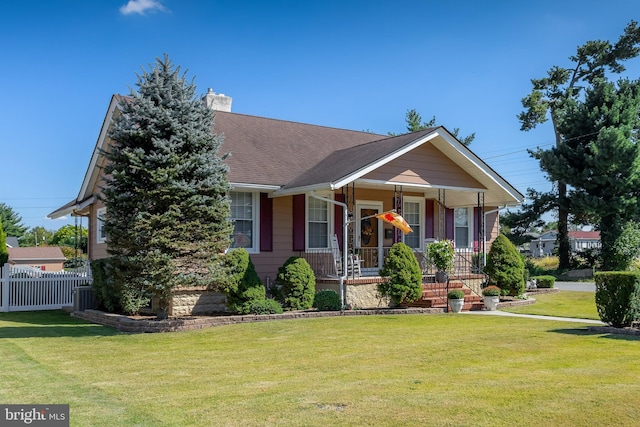 view of front of property with fence, a porch, a shingled roof, a chimney, and a front lawn