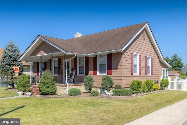 view of front of house with fence, roof with shingles, covered porch, a chimney, and a front lawn