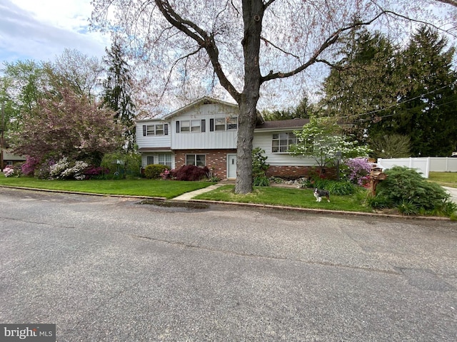 tri-level home with brick siding, a front lawn, and fence