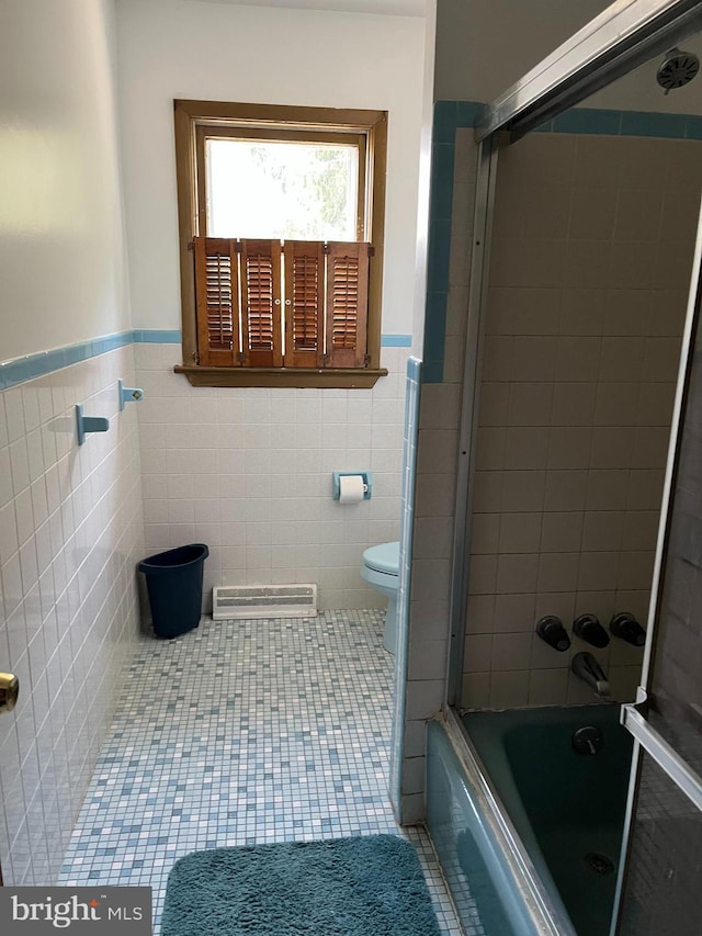 bathroom with tile patterned flooring, visible vents, toilet, combined bath / shower with glass door, and tile walls