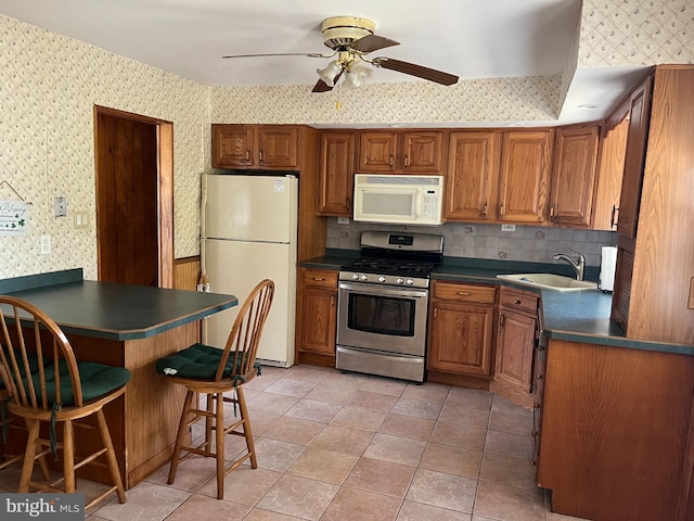 kitchen featuring wallpapered walls, white appliances, dark countertops, and a sink