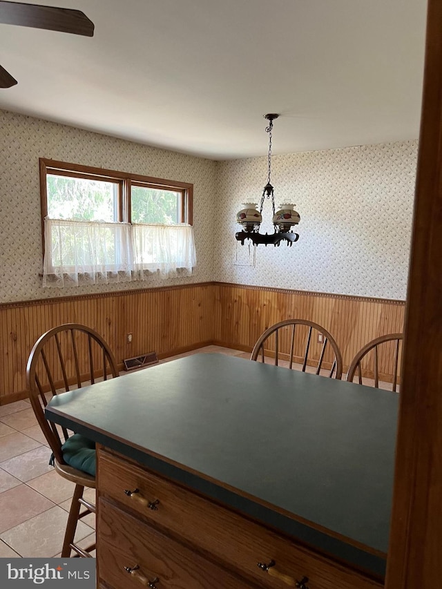 dining space with an inviting chandelier, light tile patterned flooring, wainscoting, and wallpapered walls