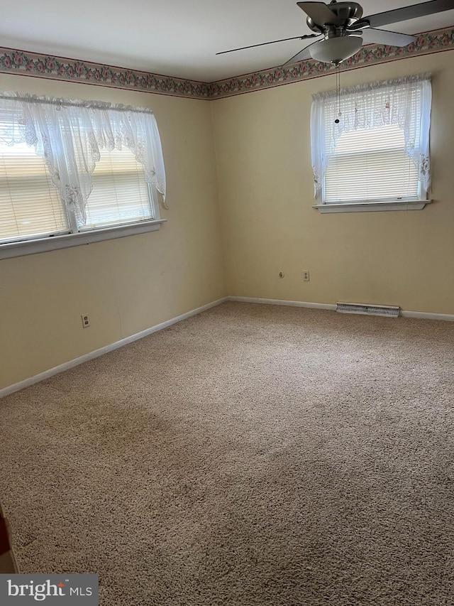 carpeted spare room with a ceiling fan, a healthy amount of sunlight, visible vents, and baseboards